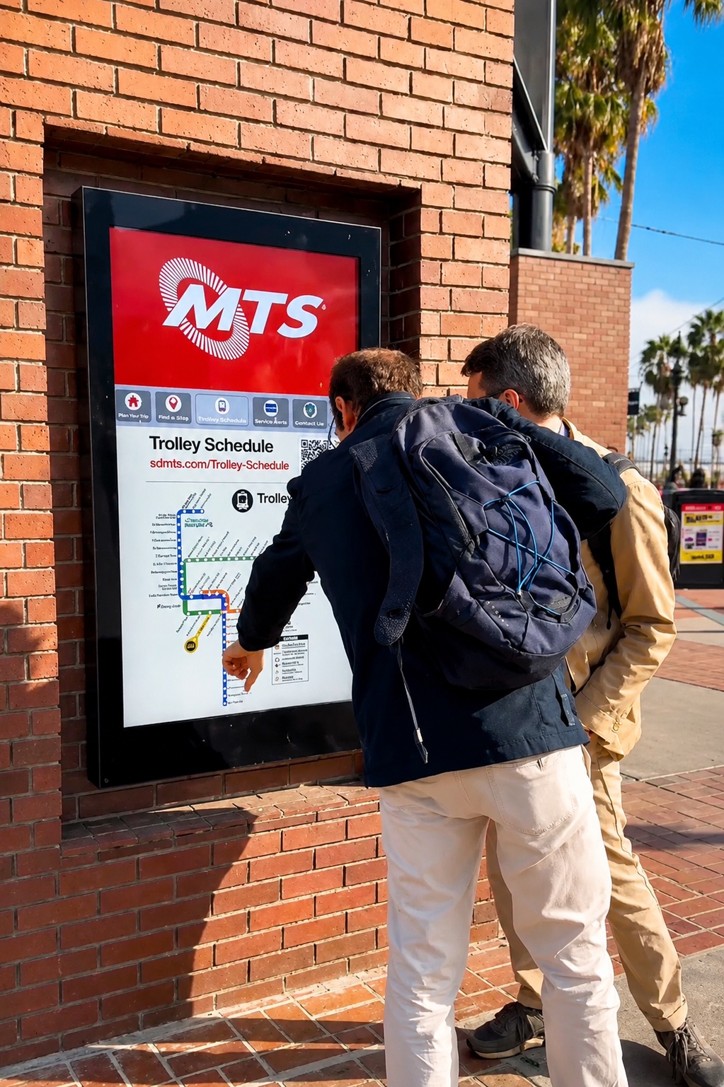 People viewing an MTS trolley schedule display mounted in brick streetscape